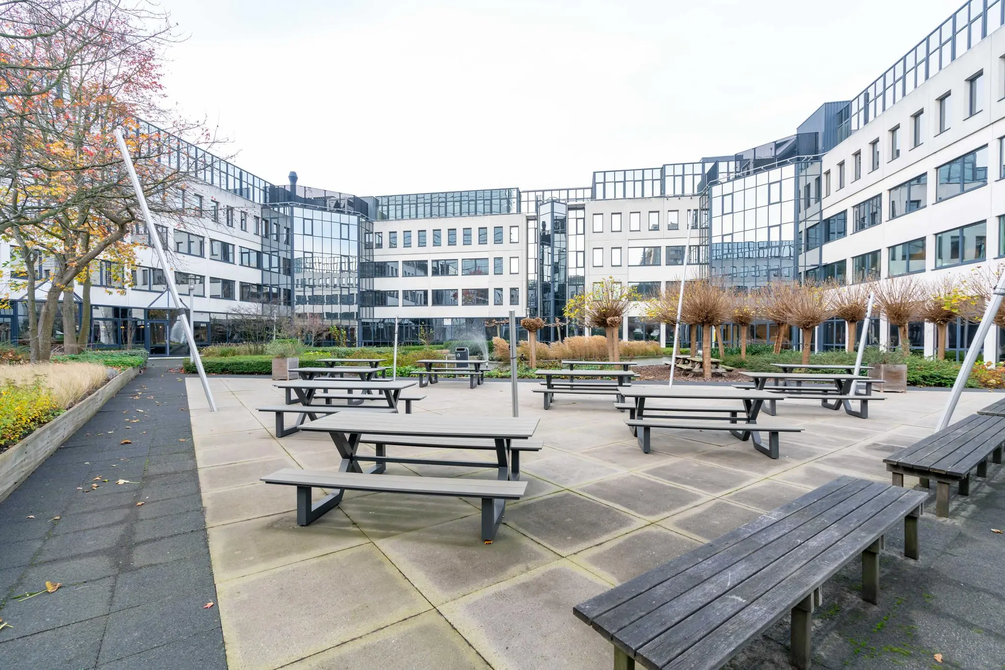 Binnenplein met picknicktafels en bomen omringd door moderne kantoorgebouwen aan de De Bruyn Kopsstraat.
